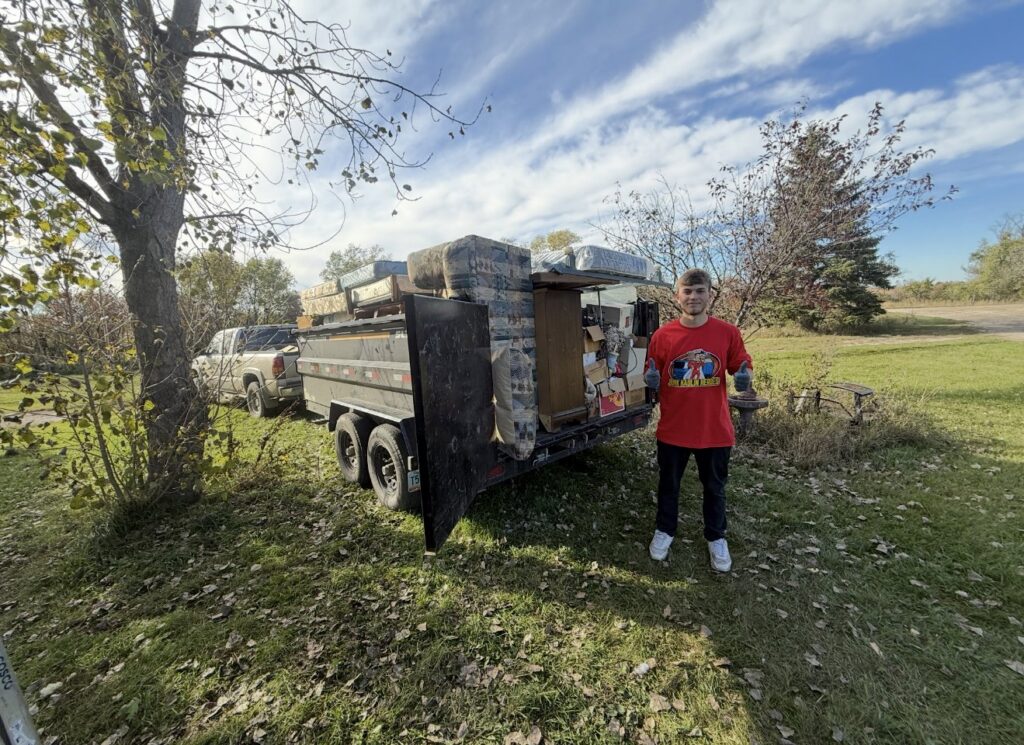 A Junk Haulin Heroes team member standing next to a trailer loaded with mattresses and other junk for removal in Bismarck, ND.