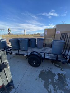 A utility trailer loaded with multiple gray trash cans, ready for transport by Hudson's Trash Removal, LLC in Great Falls, MT.