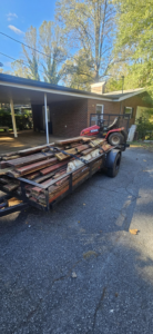 A trailer loaded with wooden planks and a riding lawnmower, ready for removal by JUNK BRO'S in Hickory, NC.