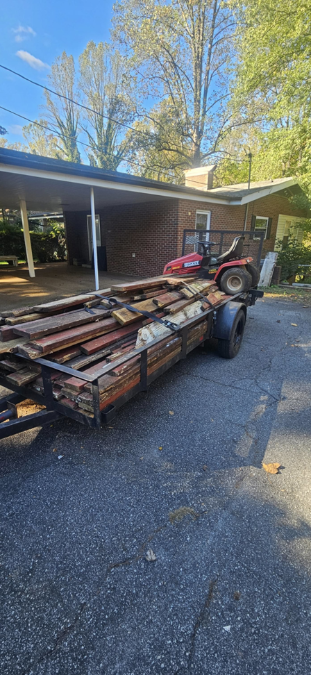 A trailer loaded with wooden planks and a riding lawnmower, ready for removal by JUNK BRO'S in Hickory, NC.