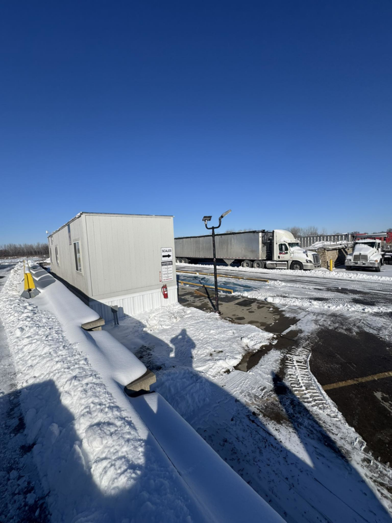 A snowy view of the Riverbend Recycling and Transfer Station yard with semi-trucks and a scale house in Independence, MO.
