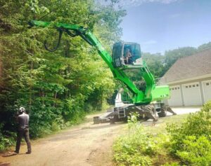 A truck transporting a green Sennebogen tree service machine on a flatbed trailer for Dark Arbor Tree Care in Portland, ME.