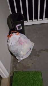 A white trash bag and a black bin on a porch, ready for A1 Valet Trash pickup in Atlanta, GA.