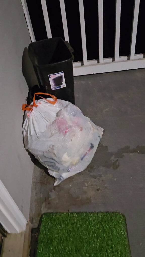 A white trash bag and a black bin on a porch, ready for A1 Valet Trash pickup in Atlanta, GA.