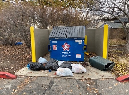 Several bags of trash and a broken green bin piled next to a dumpster, indicating a need for junk removal by United Trash Valet in Seattle, WA.