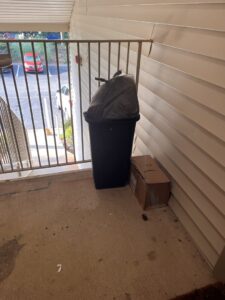 A trash bin with a black bag and a cardboard box on an apartment balcony, ready for A1 Valet Trash pickup in Atlanta, GA.