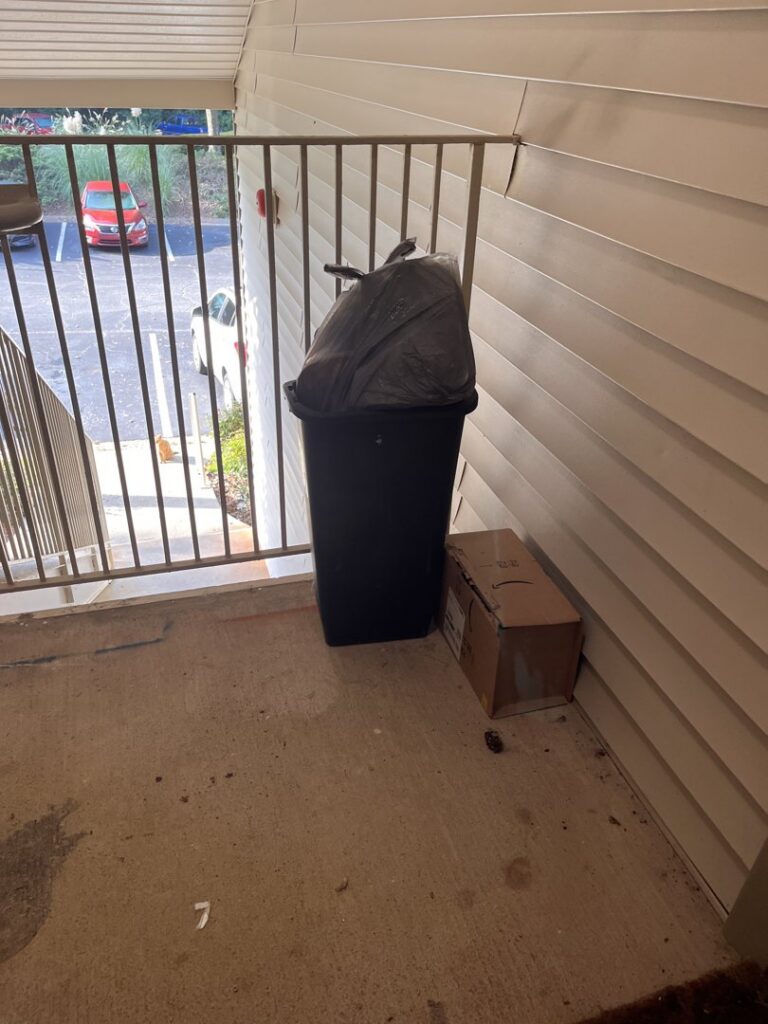 A trash bin with a black bag and a cardboard box on an apartment balcony, ready for A1 Valet Trash pickup in Atlanta, GA.