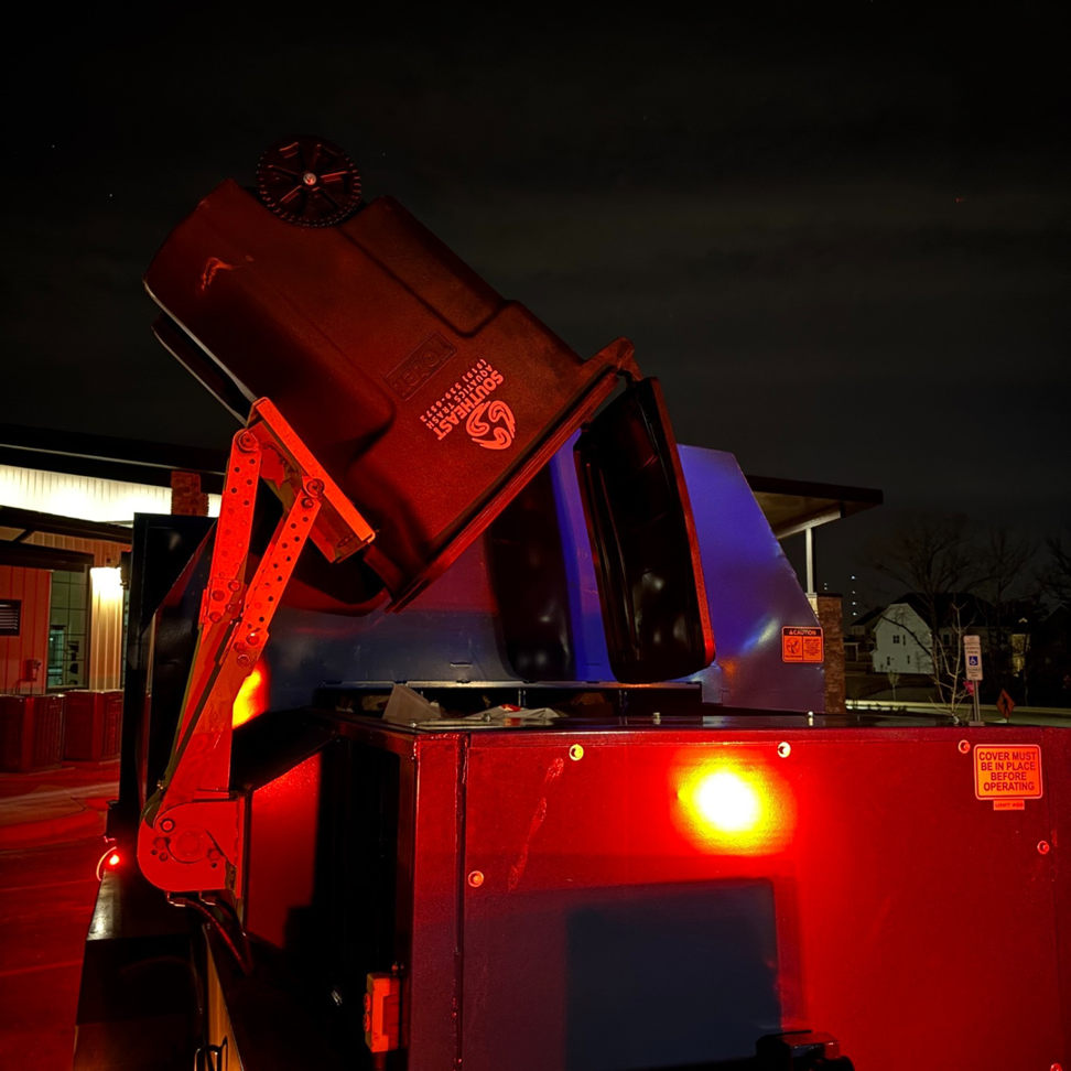 A Southeast Aquatics Trash bin being emptied into a garbage truck at night in Raleigh, NC.