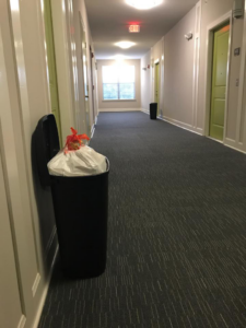 A full trash bin with a white bag ready for pickup in a residential hallway by Elite Valet Trash in Apex, NC.