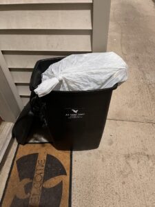 A black trash bin with a white trash bag inside, placed on a doorstep for A1 Valet Trash pickup in Atlanta, GA.