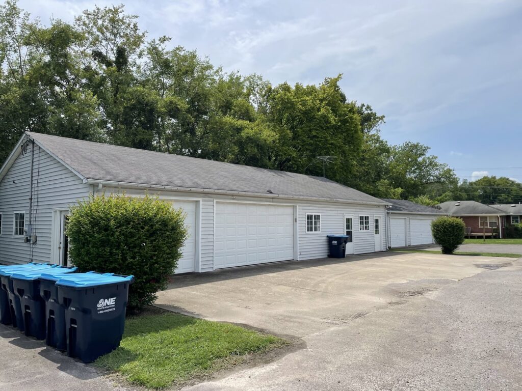 Multiple blue trash bins with the One Waste Solutions logo lined up outside a building in Murfreesboro, TN, for waste collection.