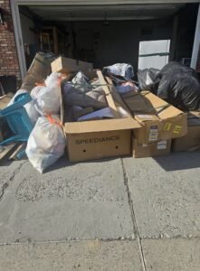 A large pile of bagged trash and cardboard boxes in front of a garage, ready for removal by Big Sky Junk Removal LLC in Billings, MT.