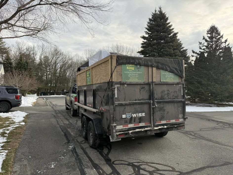 A Trash King LLC truck pulling a full junk removal trailer on a residential street in Derry, NH.
