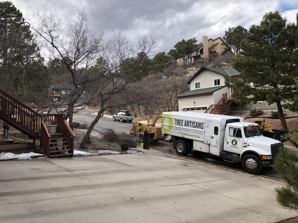 A Tree Artisans truck with a wood chipper parked on a residential driveway, ready for tree service work in Colorado Springs, CO.