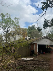 A large tree branch fallen onto a house roof and garage, showing storm damage requiring G&H Tree Service in Jackson, TN.