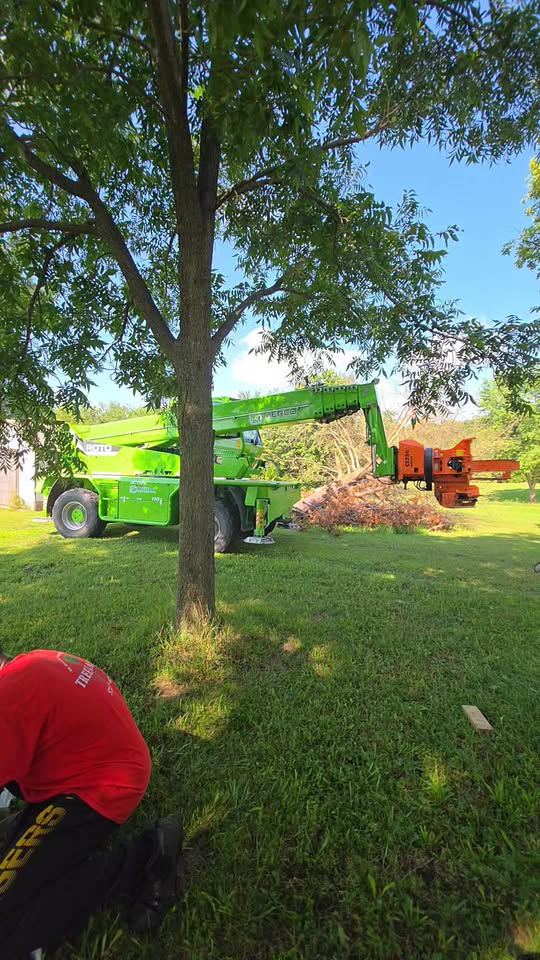 A large green tree chipper machine processing wood debris during a tree service job by Tree Masters in Columbia, MO.
