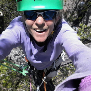 A tree climber in a helmet and harness smiling from a tree, performing services for Flygirl Trees in Albuquerque, NM.