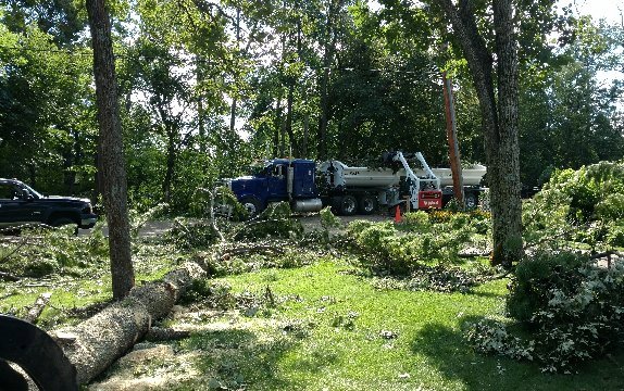 Extensive tree debris and logs on the ground after a tree removal or trimming service, with a cleanup truck in the background by K.M.C Lawn & Tree service in Peoria, IL.
