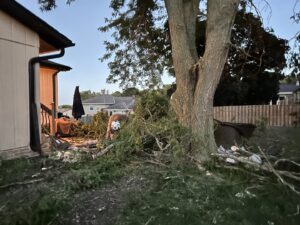 Tree branches and debris on the ground next to a house, indicating cleanup services by M S Wiekhorst Arbor Company in Columbus, NE.