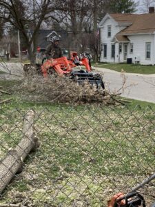 A tree service worker using a skid steer for tree debris cleanup for Father and Son Tree Service in Lansing, MI.