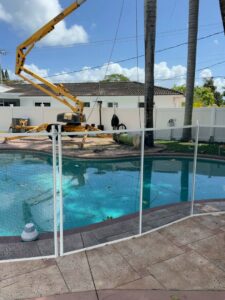 Tree debris in a residential pool after tree trimming or removal work, with a bucket lift in the background, by OnTop Tree Service in Miami, FL