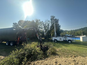 A grapple truck loads tree debris into a trailer with a bucket truck nearby for 4M Tree Service in Knoxville, TN.