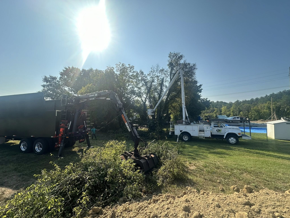 A grapple truck loads tree debris into a trailer with a bucket truck nearby for 4M Tree Service in Knoxville, TN.