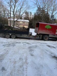 A trailer loaded with tree debris and a chipper truck with a tree service logo from BlueWater Tree Service, LLC in Bangor, ME.