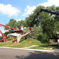 Tree service workers using a bucket truck and crane to remove a large fallen tree near a house by Ballard Enterprises in Crownsville, MD.