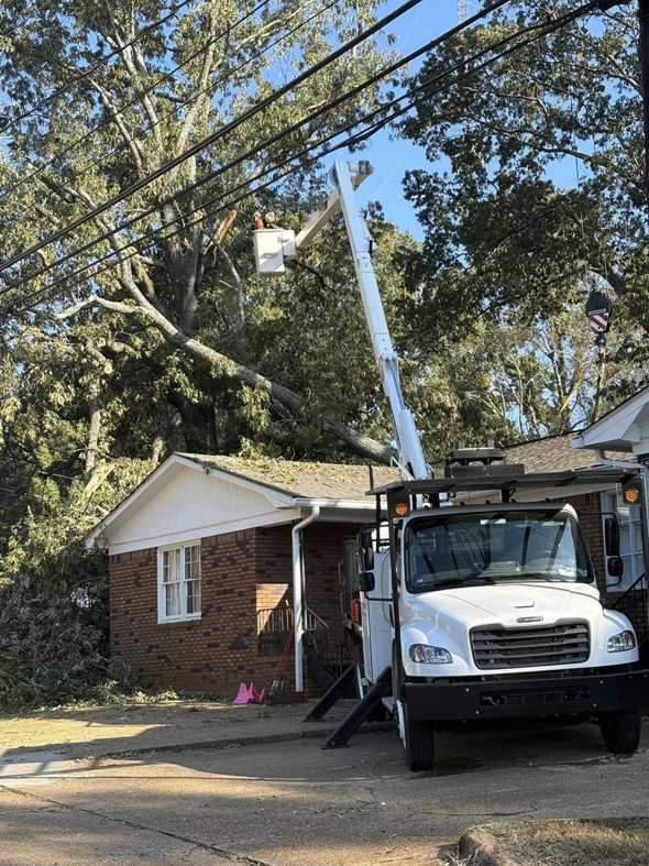 A tree service worker in a bucket truck removing a large fallen tree branch from a house roof by Triple J Tree Service, LLC in Tuscaloosa, AL.