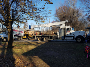 A crane truck, wood chipper, and logs on a flatbed truck during a tree removal job by Climb-Ax Tree Service in Louisville, KY