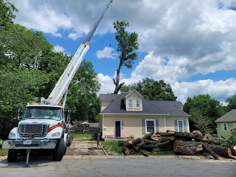 A worker on a tree being removed by a crane over a house by Perez Landscape and Tree Services in Kansas City, MO.