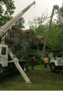 Two crane trucks and a crew performing tree removal services near an old house for State Tree Services, Inc in Sumter, SC.