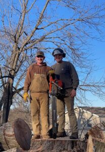 A professional tree removal crew with a chainsaw standing on a large stump, ready for the next job by Capital Tree Company in Des Moines, IA.