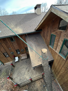 A tree removal job in progress next to a residential house, showing a cut tree trunk with ropes, by Superior Tree and Stump LLC in Topeka, KS.