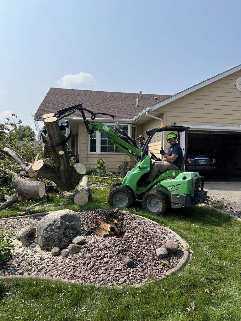 A Patriot Tree Service worker operating a mini-loader to clear tree sections after removal in Sioux Falls, SD