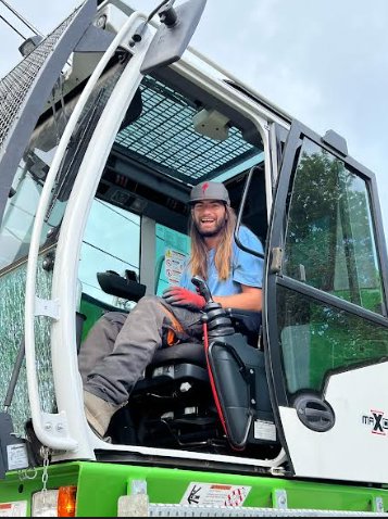 A green Sennebogen machine performing tree removal near a residential property for Dark Arbor Tree Care in Portland, ME.