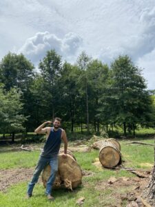 A tree service worker standing proudly next to large logs after a tree removal job by Sunny Meadows Land and Tree LLC in Birmingham, AL