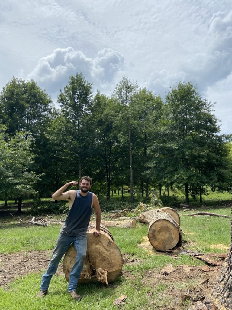 A tree service worker standing proudly next to large logs after a tree removal job by Sunny Meadows Land and Tree LLC in Birmingham, AL