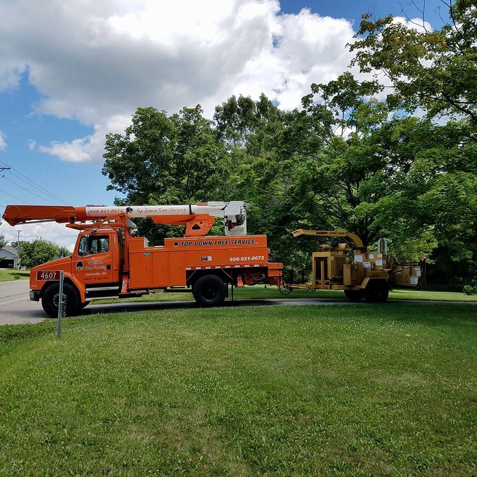 An orange tree service bucket truck with a wood chipper attached, used by Top Down Tree Service LLC in Janesville, WI