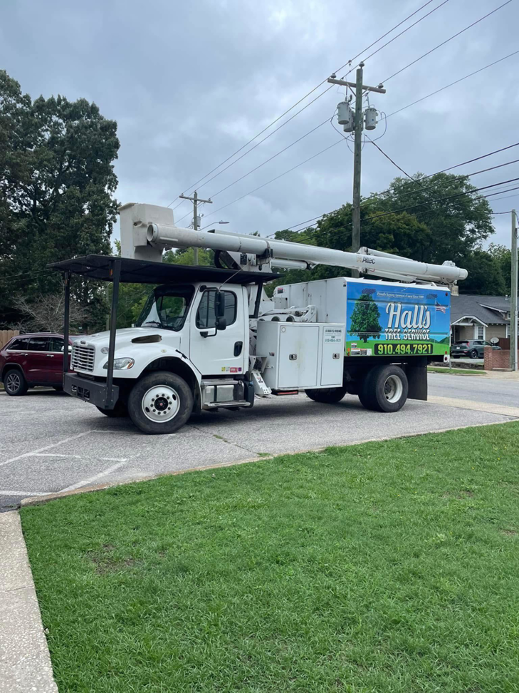A white bucket truck with Hall's Tree Service, INC logo parked on a street in Fayetteville, NC.