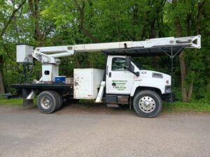A white tree service bucket truck with the company logo parked on a road for The Tree Service in Knoxville, TN.