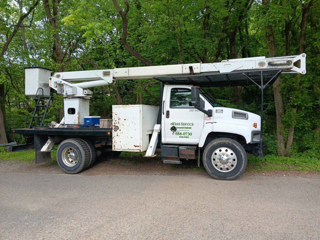 A white tree service bucket truck with the company logo parked on a road for The Tree Service in Knoxville, TN.