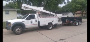 A tree service bucket truck with a trailer attached, used by Grand Island Tree Service in Grand Island, NE.