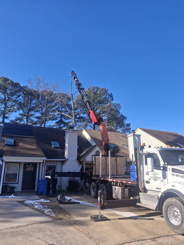 A tree service crane truck positioned in front of a residential home for tree work by Alley's Tree Service in Va Beach, VA.