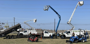 A tree service crew standing with their bucket trucks, trailer, and equipment at JRs PALM TREE SERV. in Corpus Christi, TX.