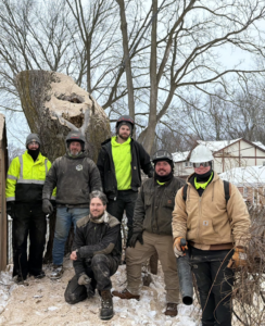 A tree service crew standing next to a large tree stump after a removal job by J's Tree Trimming and Removal, Inc. in Ann Arbor, MI.