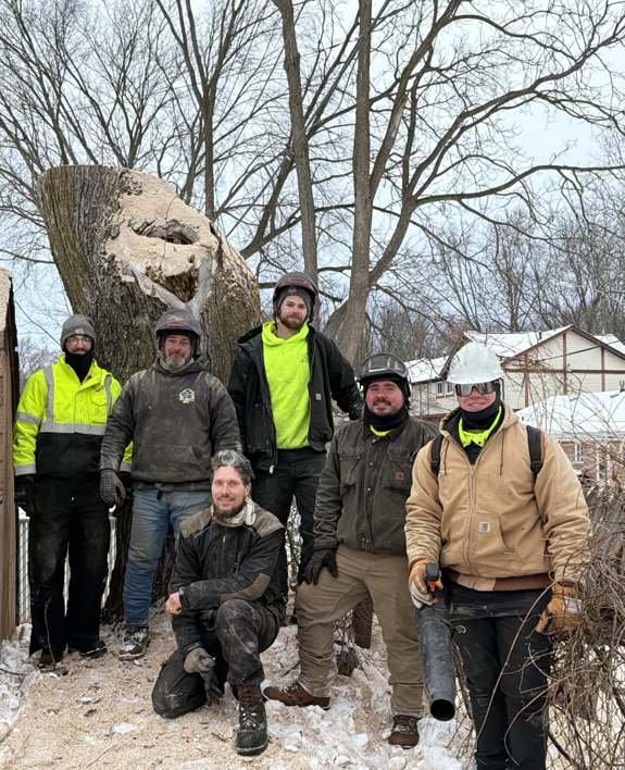 A tree service crew standing next to a large tree stump after a removal job by J's Tree Trimming and Removal, Inc. in Ann Arbor, MI.