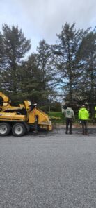 A tree service crew operating a wood chipper to process felled trees on a paved area for Teacher's Tree Service in South Burlington, VT.