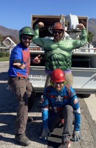 The My Tree Guys, LLC crew in superhero costumes and helmets in front of a tree service truck in Salt Lake City, UT.